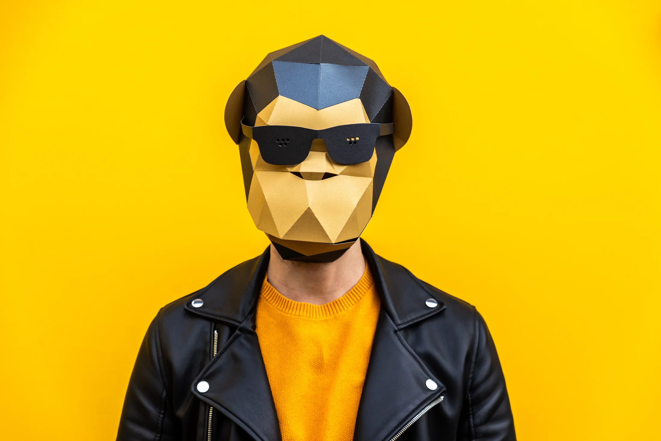 Person wearing a geometric animal mask and sunglasses against a yellow background