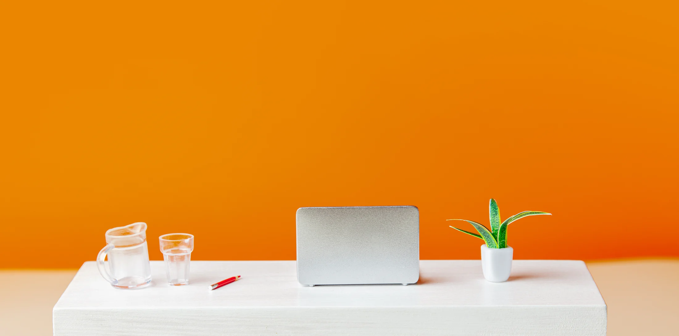 Laptop and desk accessories arranged against an orange wall Laptop and desk accessories arranged against an orange wall