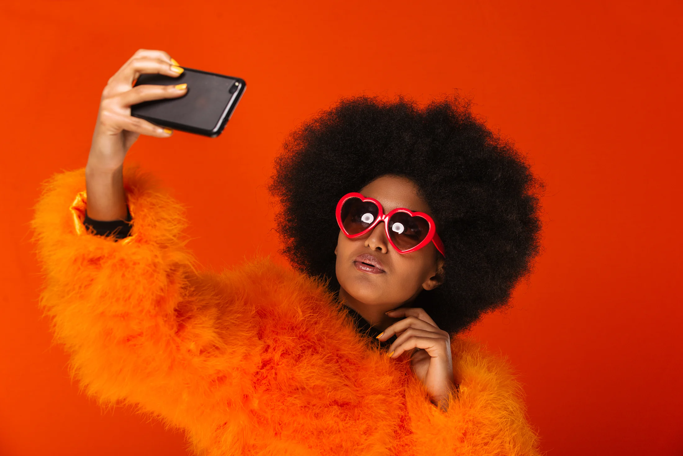 Woman wearing red sunglasses taking a selfie against an orange background