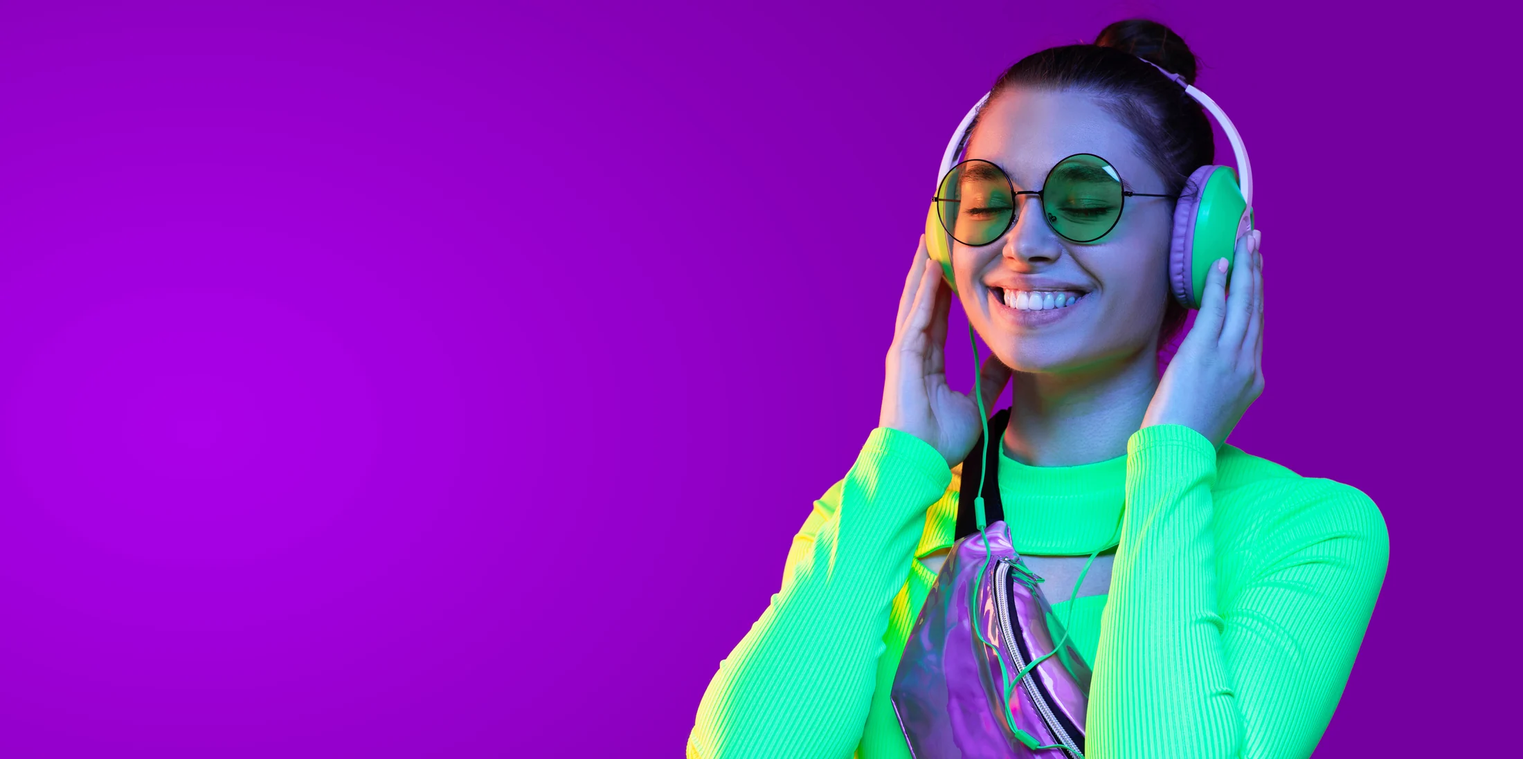 Woman in glasses enjoying music through headphones under colourful lighting