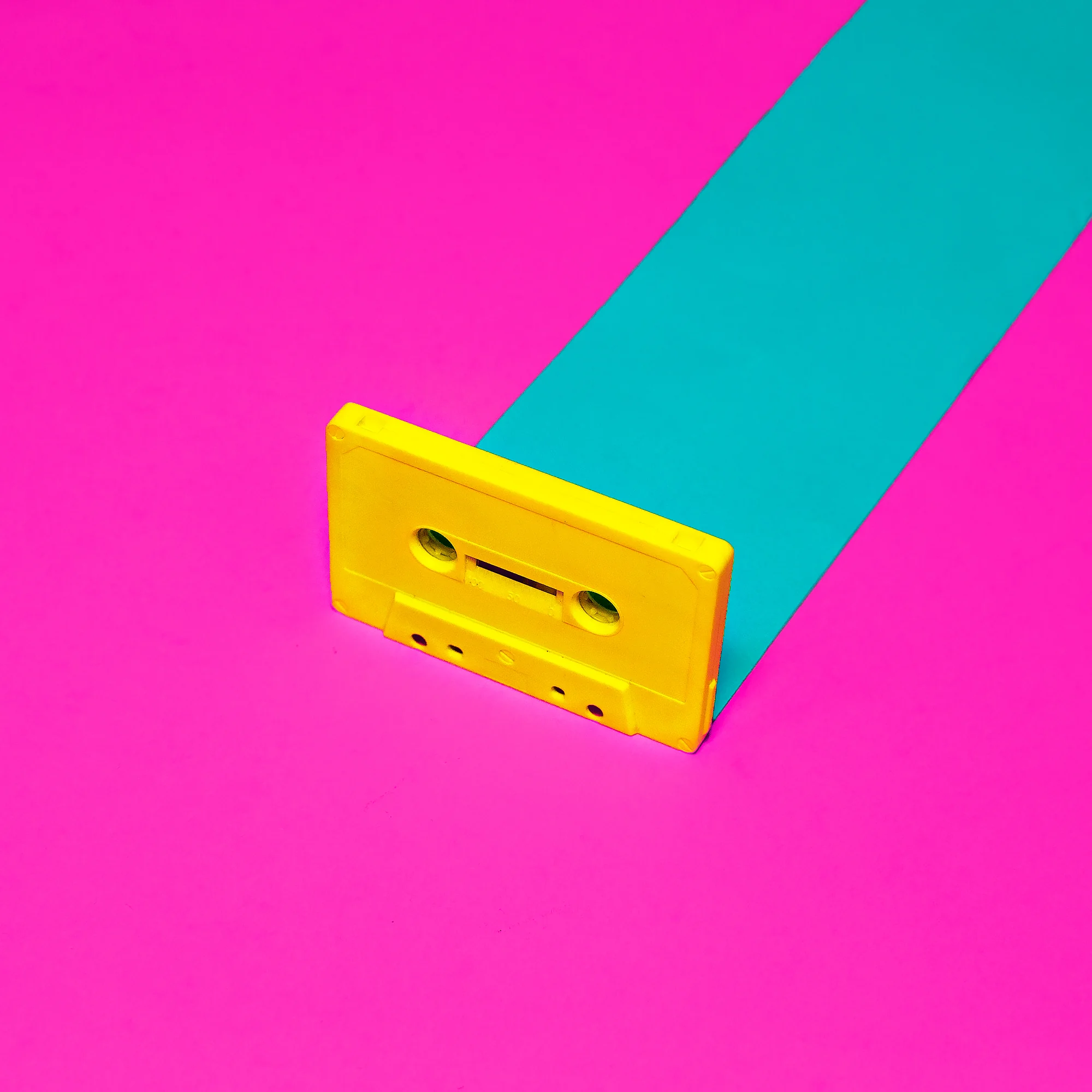 Yellow cassette tape against contrasting pink and turquoise paper Yellow cassette tape against contrasting pink and turquoise paper