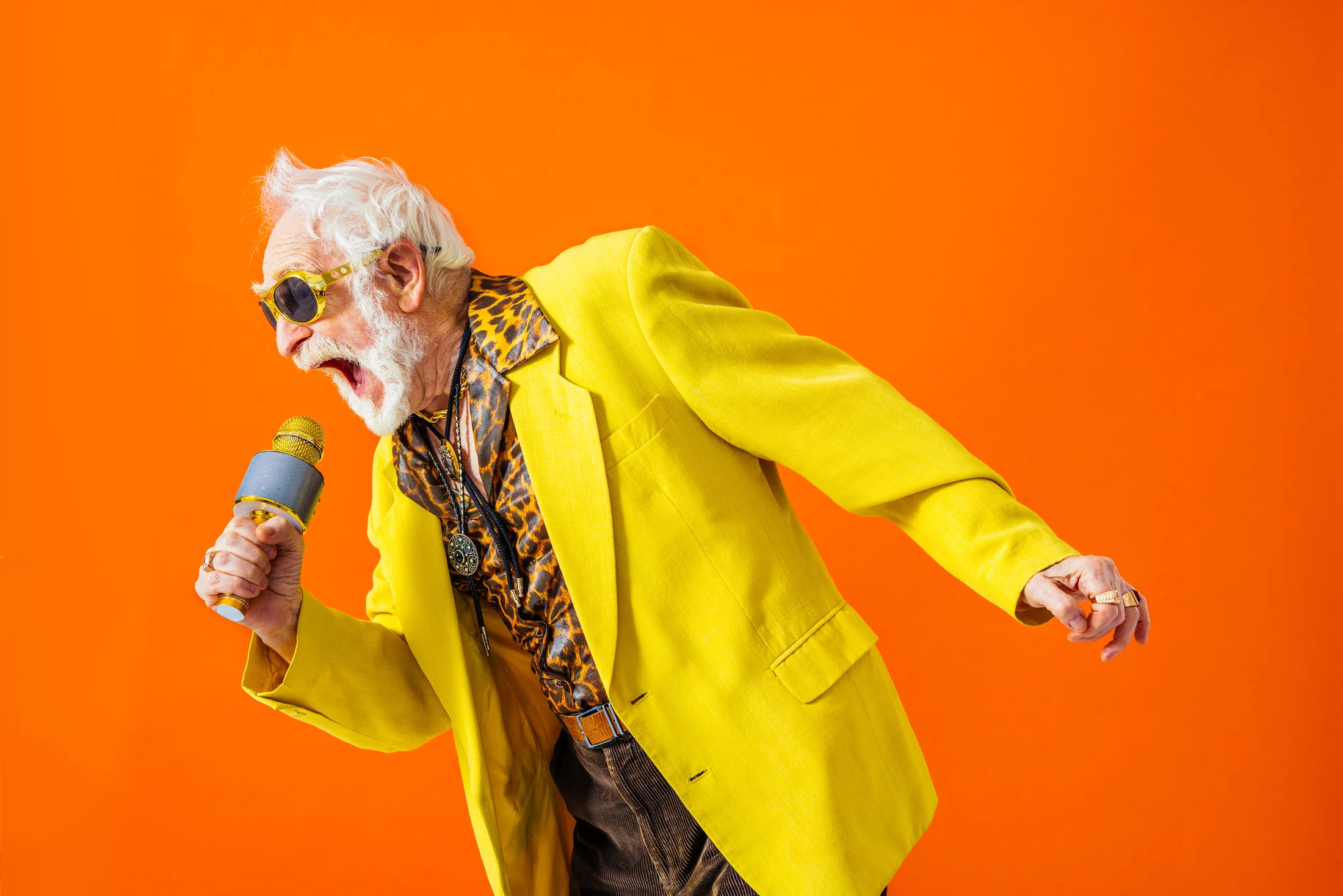 Man in a yellow jacket singing into a microphone against an orange background
