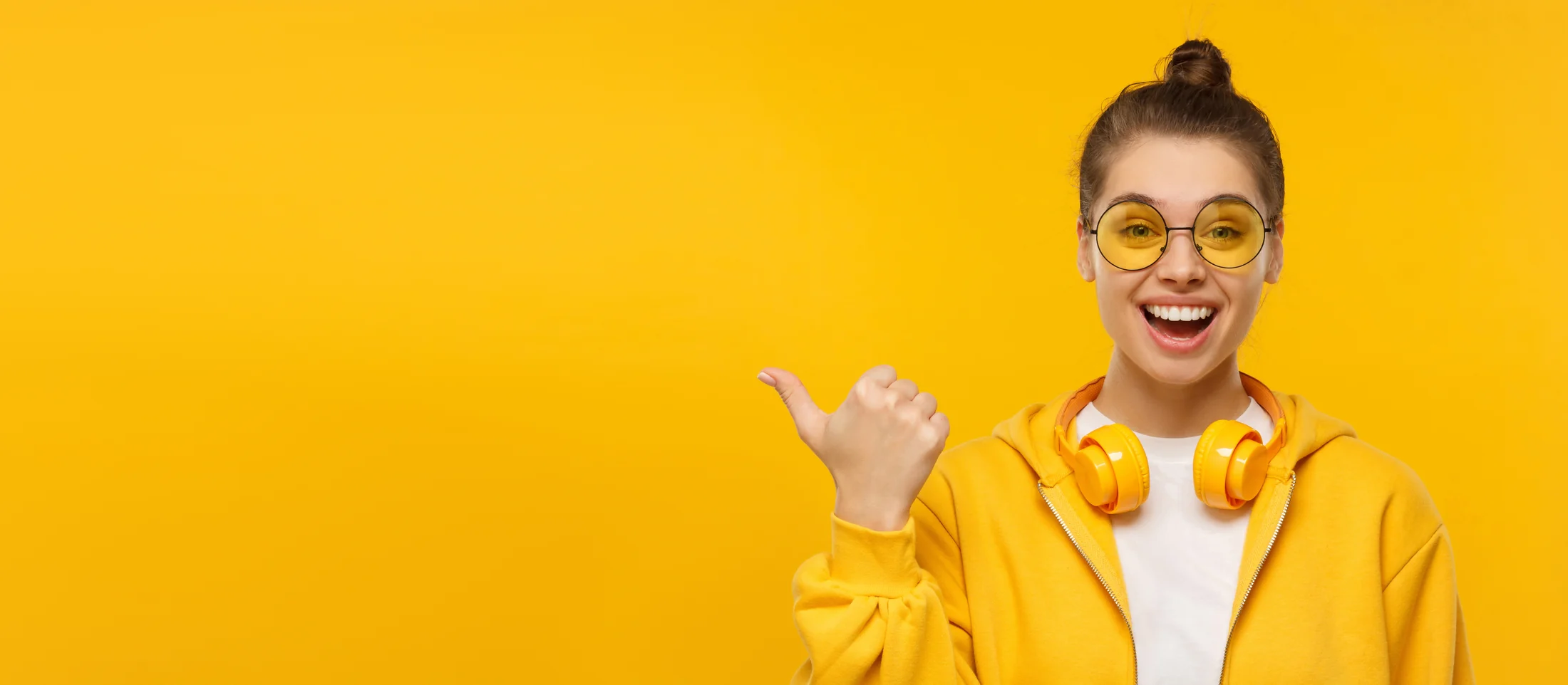 Woman with yellow headphones gesturing towards open space on a yellow background