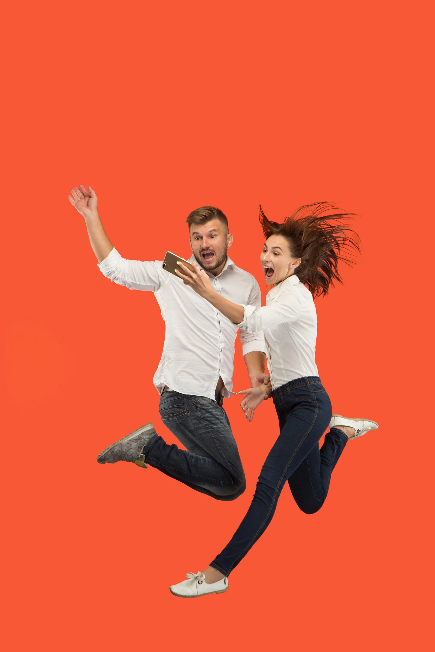 Two people jumping against a bright coral background