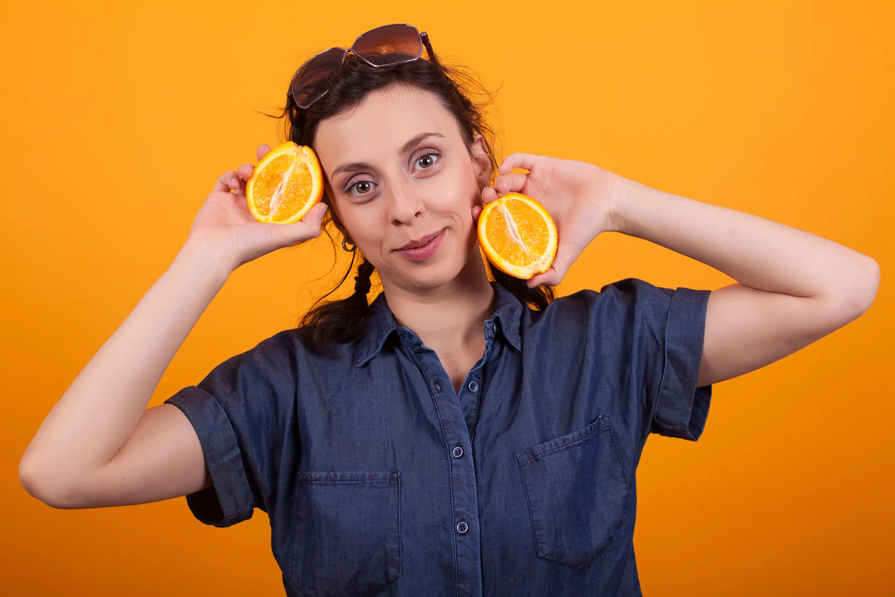 Woman Holds Orange Halves on Orange Background