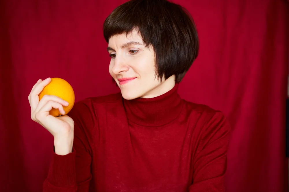 Woman Holding an Orange Against a Red Background