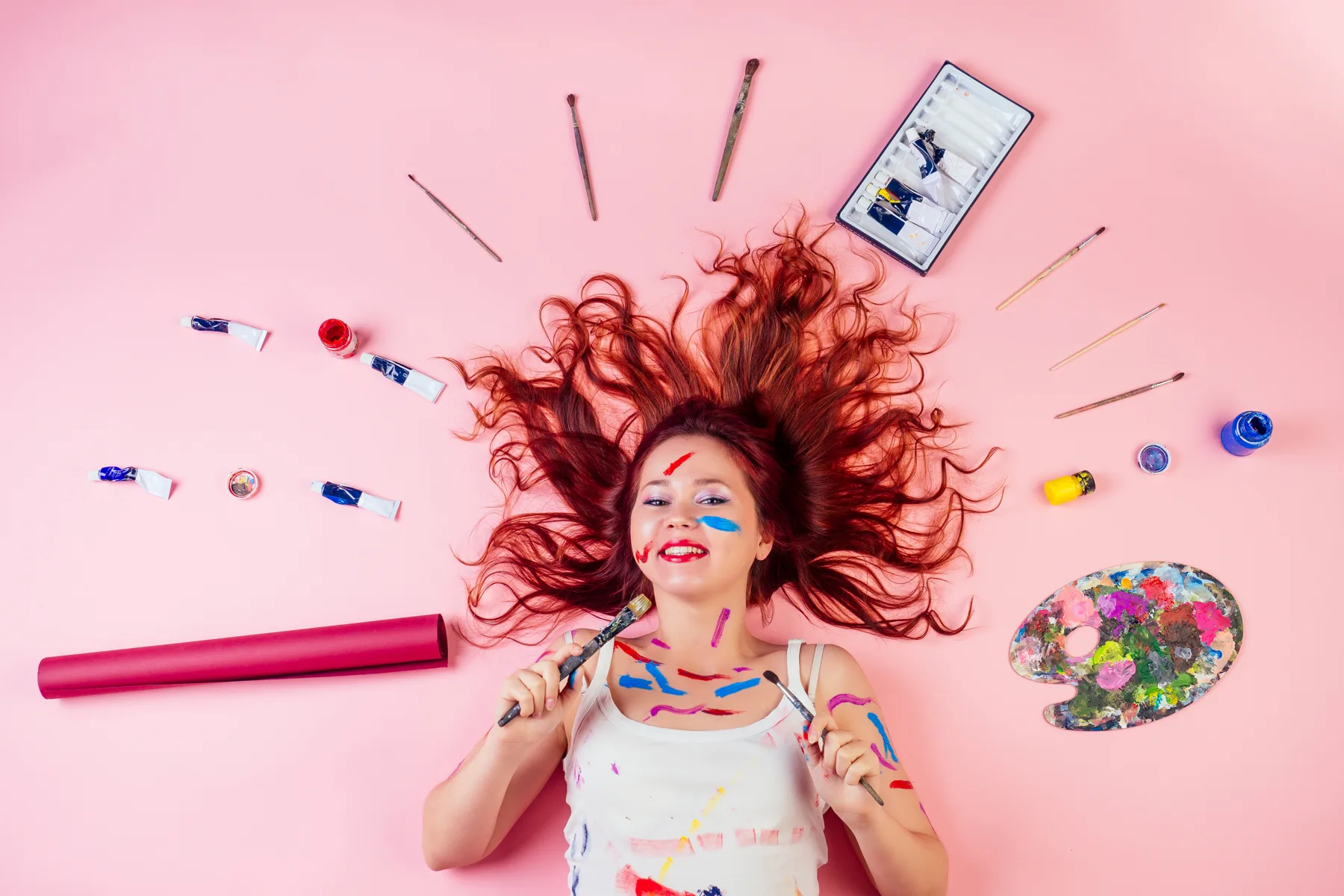 Woman Lying Surrounded By Painting Supplies On Pink Woman Lying Surrounded By Painting Supplies On Pink