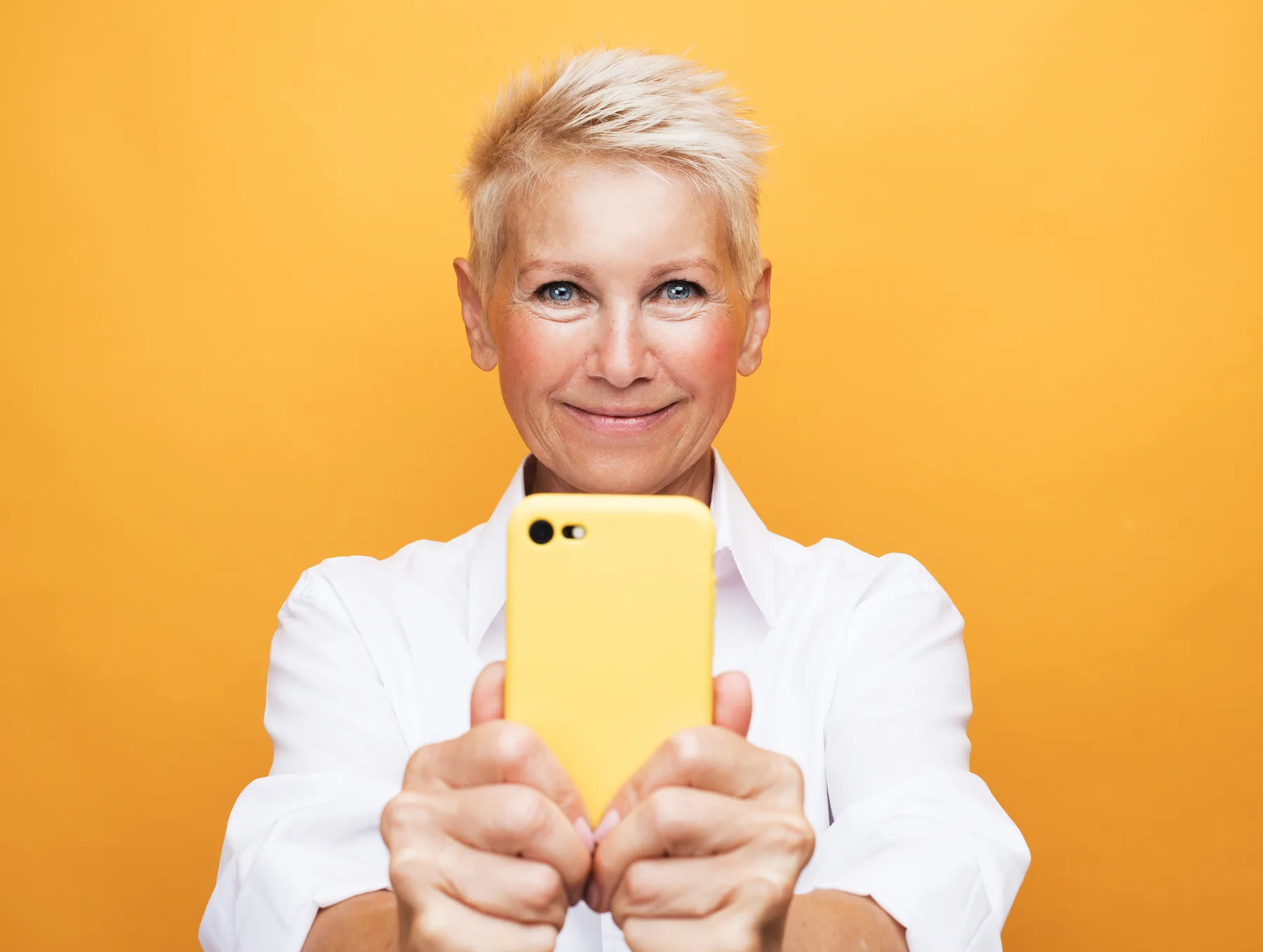 Smiling Woman Holding Yellow Cellphone on Yellow Background