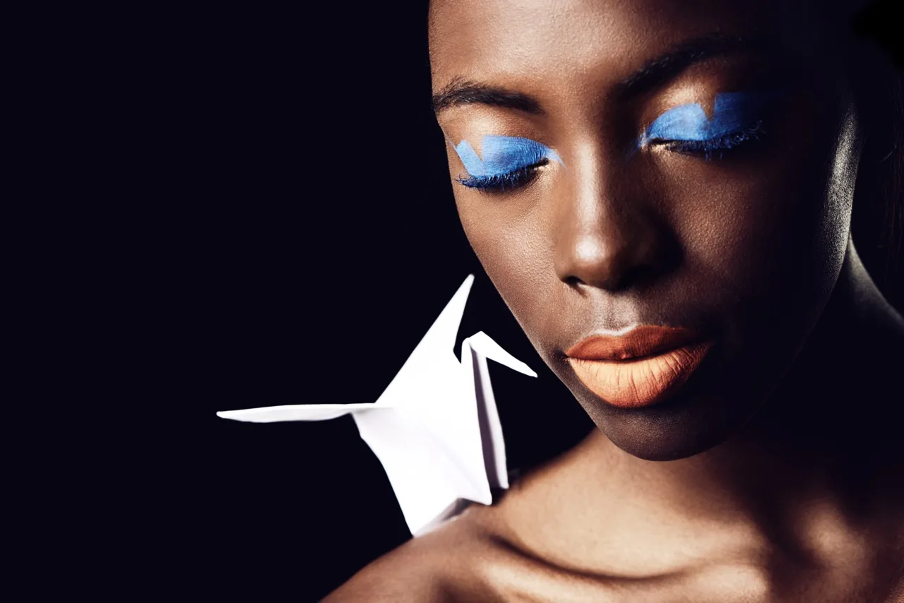 Editorial portrait with blue eye makeup and a white origami bird